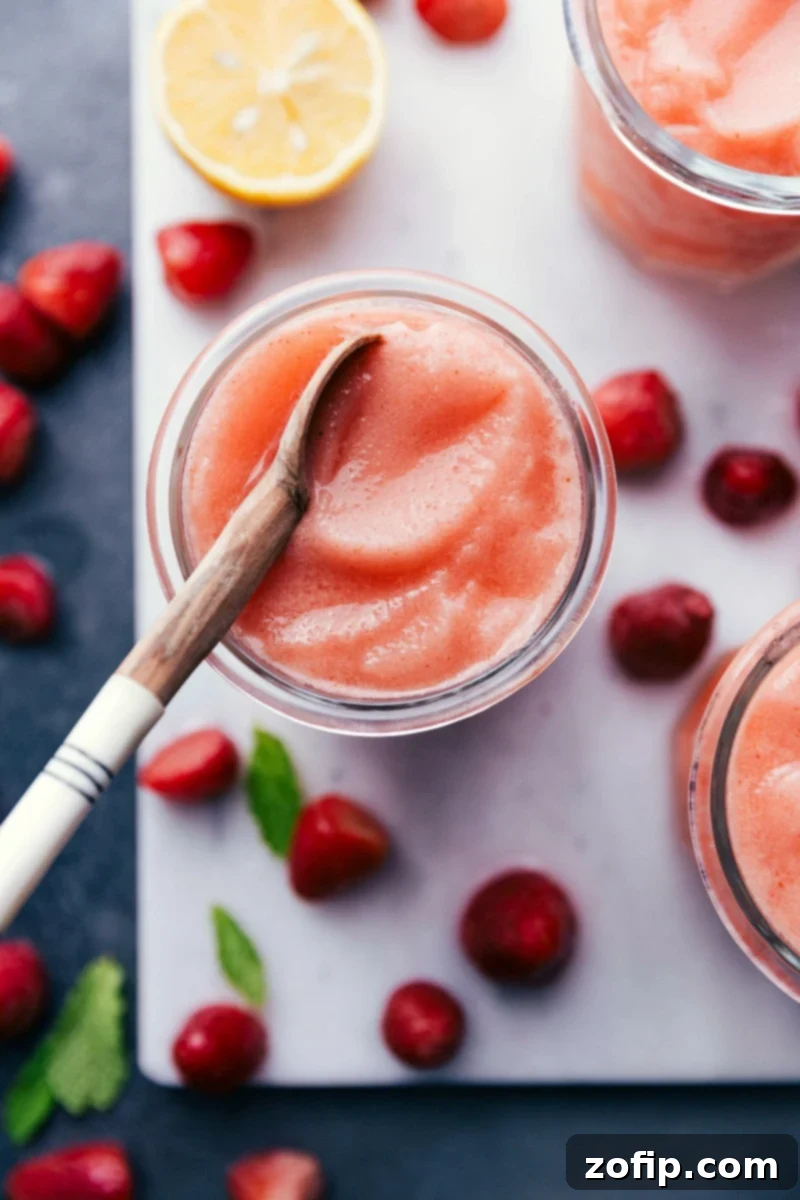 A frosty glass of homemade Lemon Berry Slush, garnished with fresh berries and a slice of lemon, ready to be enjoyed with a spoon.