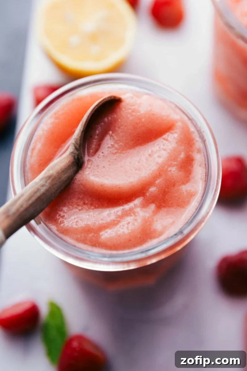 A beautifully presented, ice-cold Lemon Berry Slush in a glass, garnished with fresh strawberries and vibrant mint leaves, set on a rustic surface.
