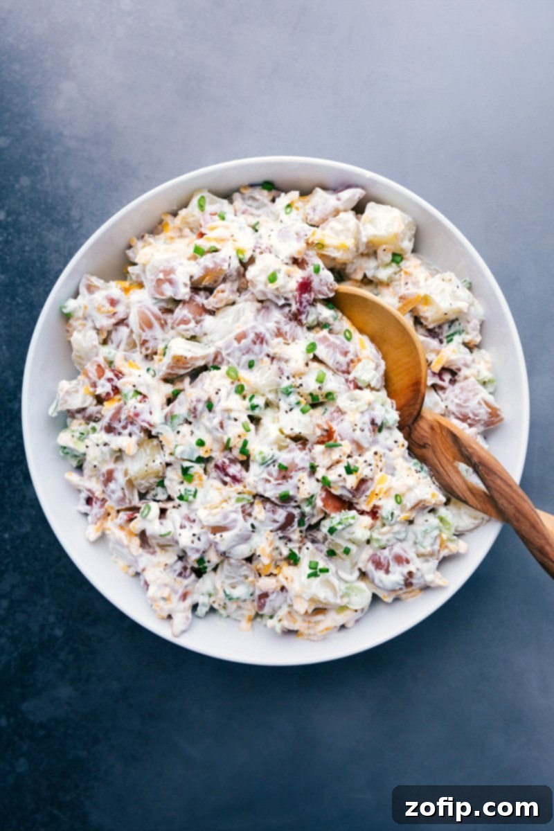 Large bowl of creamy ranch potato salad, delicious and ready to serve, garnished with fresh green onions and crispy bacon.