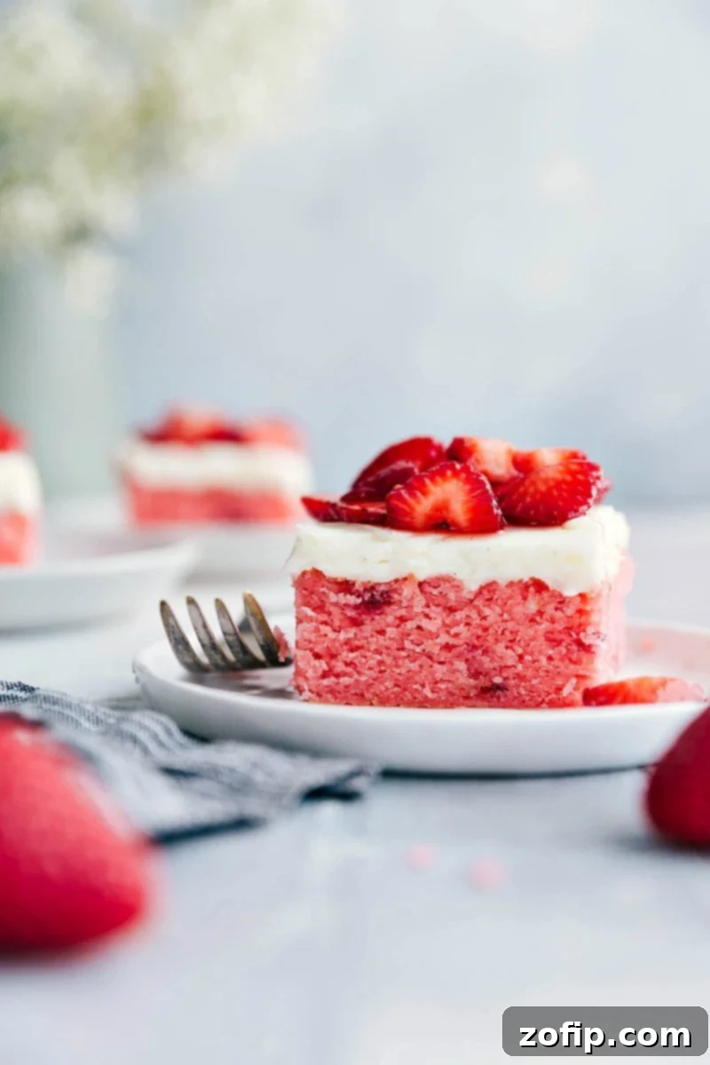 The best homemade Strawberries and Cream Cake with thick cream cheese frosting and sugared strawberries. A beautiful slice of homemade Strawberries and Cream Cake on a plate, garnished with fresh sugared strawberries and a spoon, ready to be enjoyed.