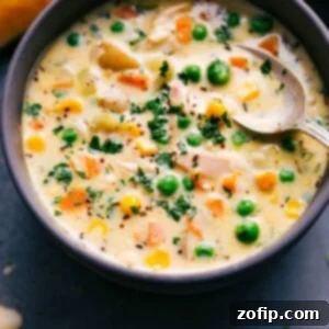 A square image of a bowl of Chicken Pot Pie Soup, topped with puff pastry and fresh herbs.