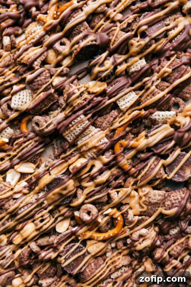 The finished Chocolate Peanut Butter Snack Mix, featuring a generous drizzle of chocolate and peanut butter, invitingly spread on a parchment-lined sheet pan, ready to be broken and enjoyed.
