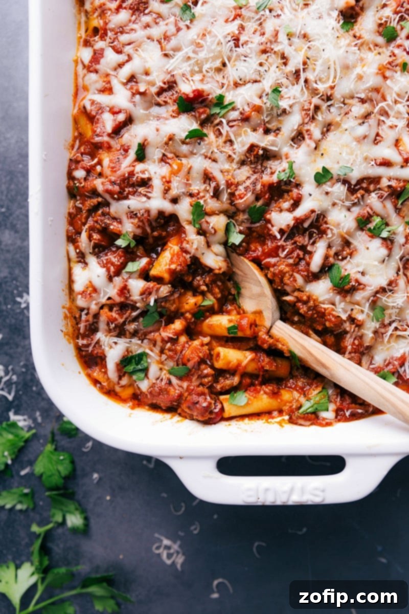 Warm and Delicious Baked Ziti Ready to Serve A warm, gooey baked ziti casserole dish, with a serving scooped out revealing layers of pasta, meat sauce, and melted cheese.