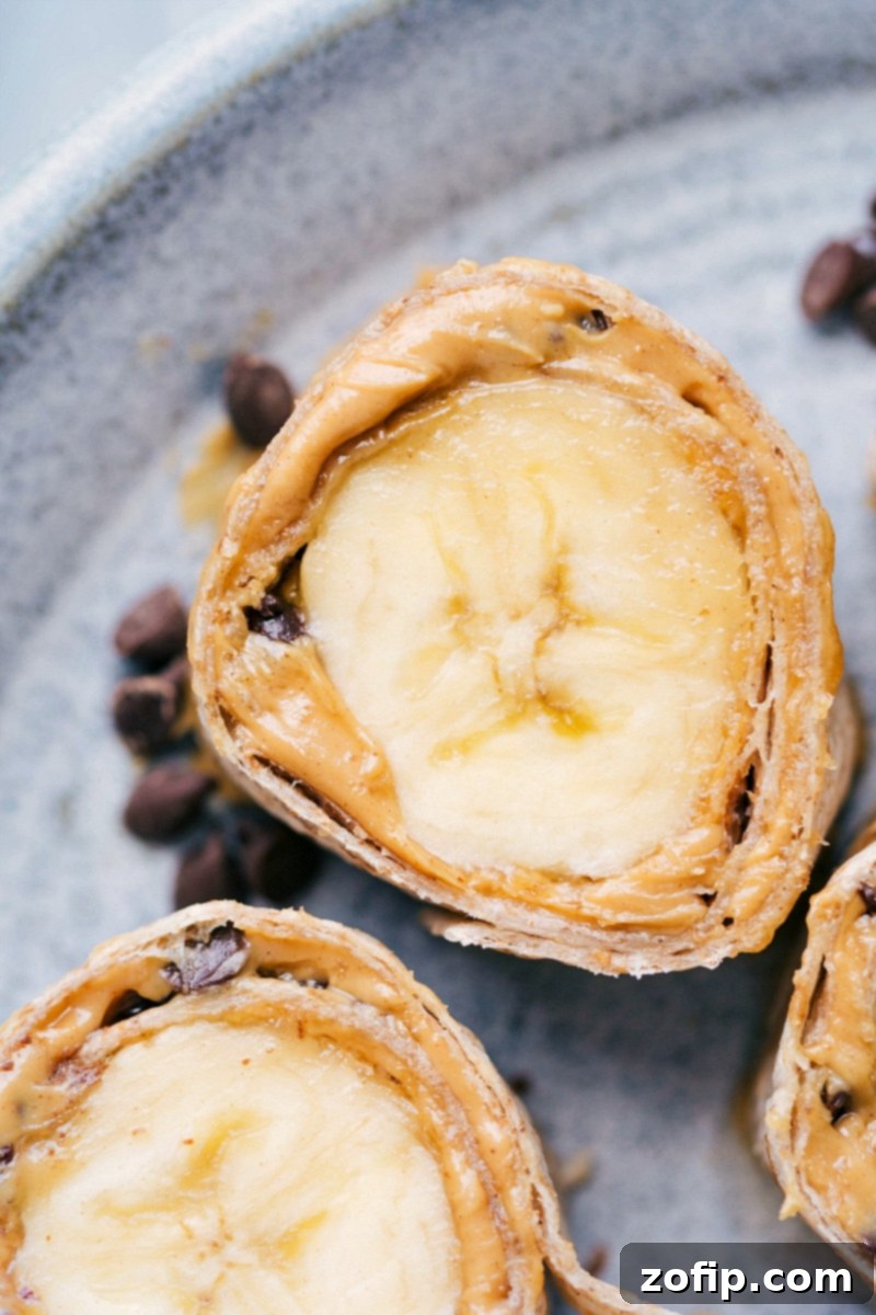 Detailed cross-section view of a Banana Sushi Bite, revealing layers of tortilla, peanut butter, granola, and fresh banana in a delightful spiral.