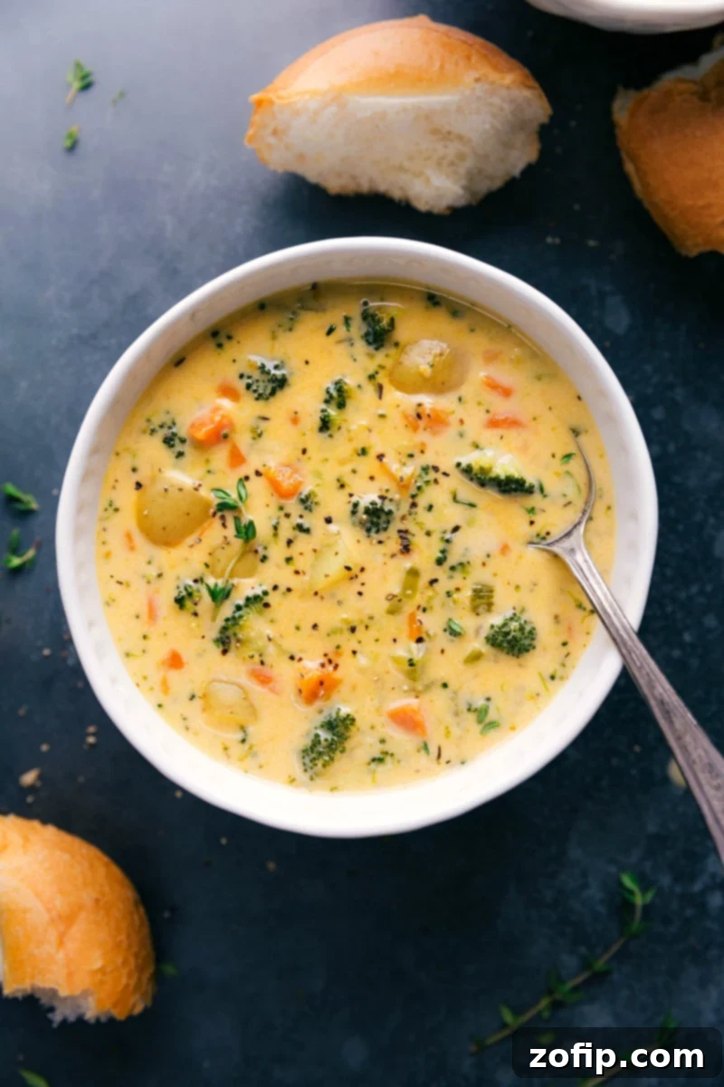 This creamy, hearty Broccoli Potato Soup is loaded with crisp-tender broccoli, golden buttery potatoes, and even more veggies. On a cold, drizzly day, there's nothing like enjoying this soup served in a crusty sourdough bread bowl or with dinner rolls for dipping! Recipe via ChelseasMessyApron.com #broccolisoup #potato #broccoli #soup #warming #wintery Big bowl of Creamy Potato Broccoli Cheese Soup, garnished with fresh herbs.