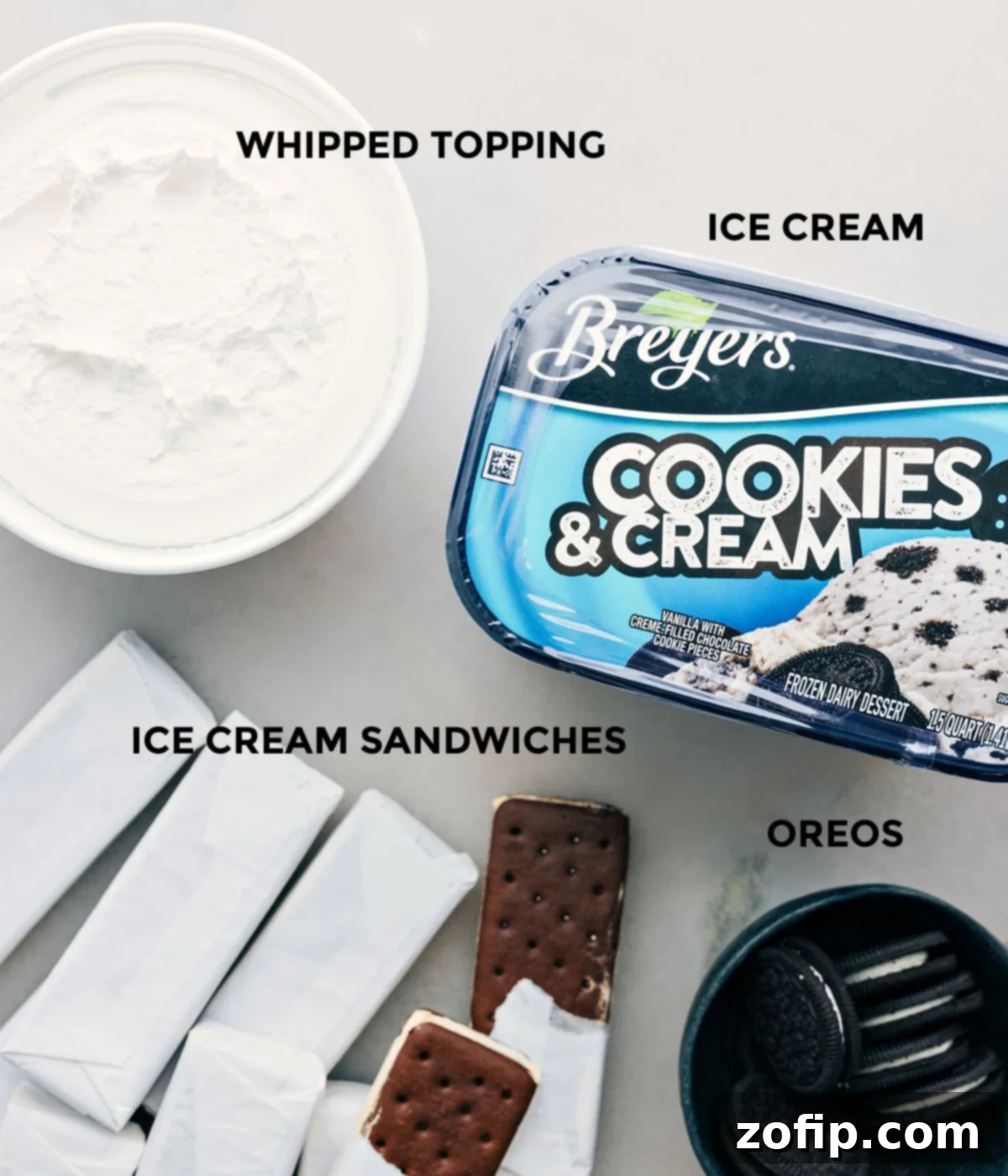 Ice Cream Sandwich Dream 3 All four essential ingredients for the Ice Cream Sandwich Cake laid out neatly on a surface: vanilla ice cream sandwiches, a tub of cookies and cream ice cream, a container of frozen whipped topping, and a pack of Oreo cookies ready for crushing.