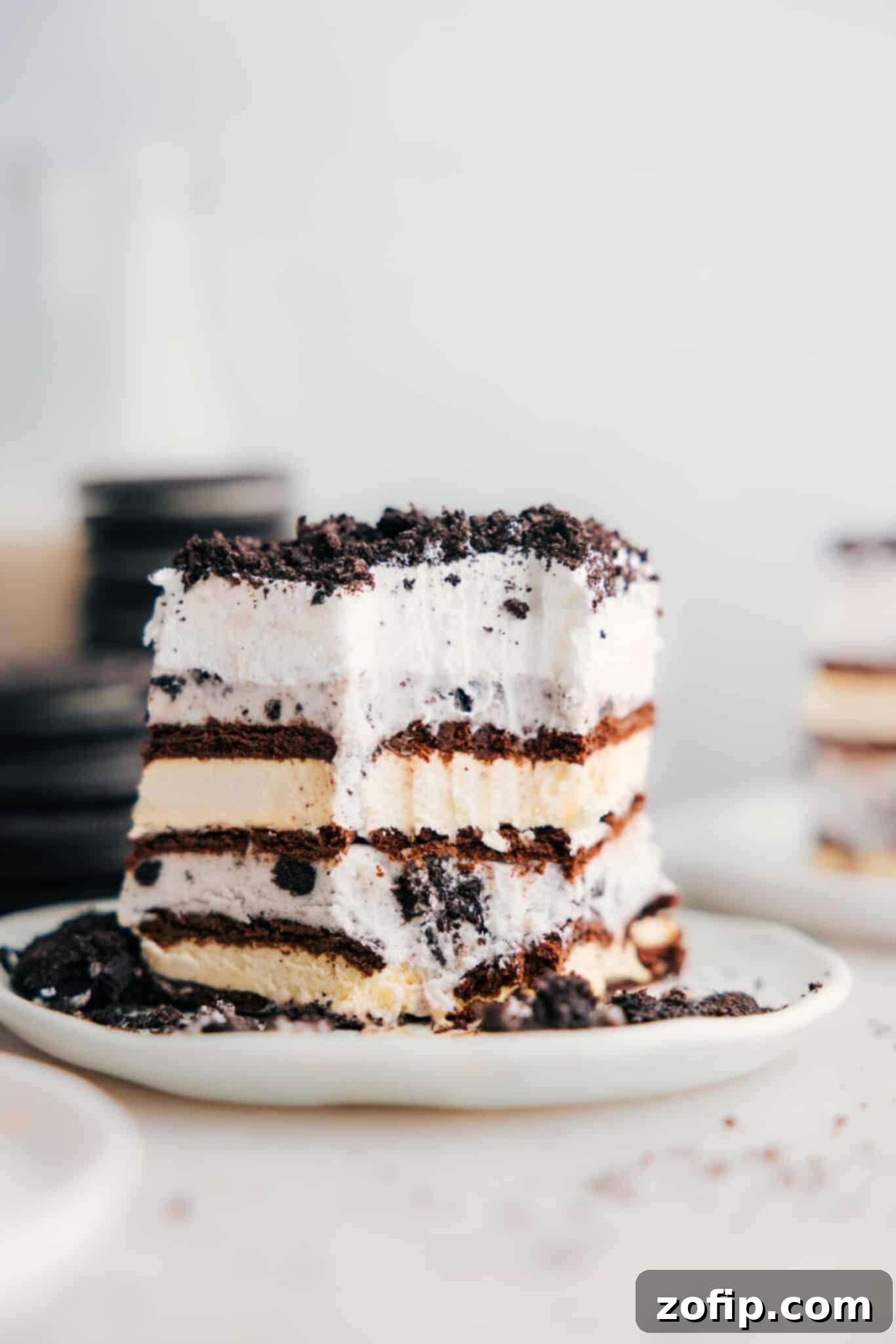 Ice Cream Sandwich Dream 7 A large, perfectly cut slice of Ice Cream Sandwich Cake with a bite taken out, revealing the distinct and beautifully layered components: chocolate cookie, vanilla ice cream, cookies and cream ice cream, and a fluffy whipped topping.
