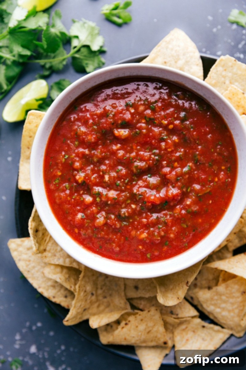 The finished homemade restaurant-style salsa recipe in a beautiful ceramic bowl, garnished with fresh cilantro, ready to be served with crunchy tortilla chips on the side, showcasing its fresh and vibrant flavors.