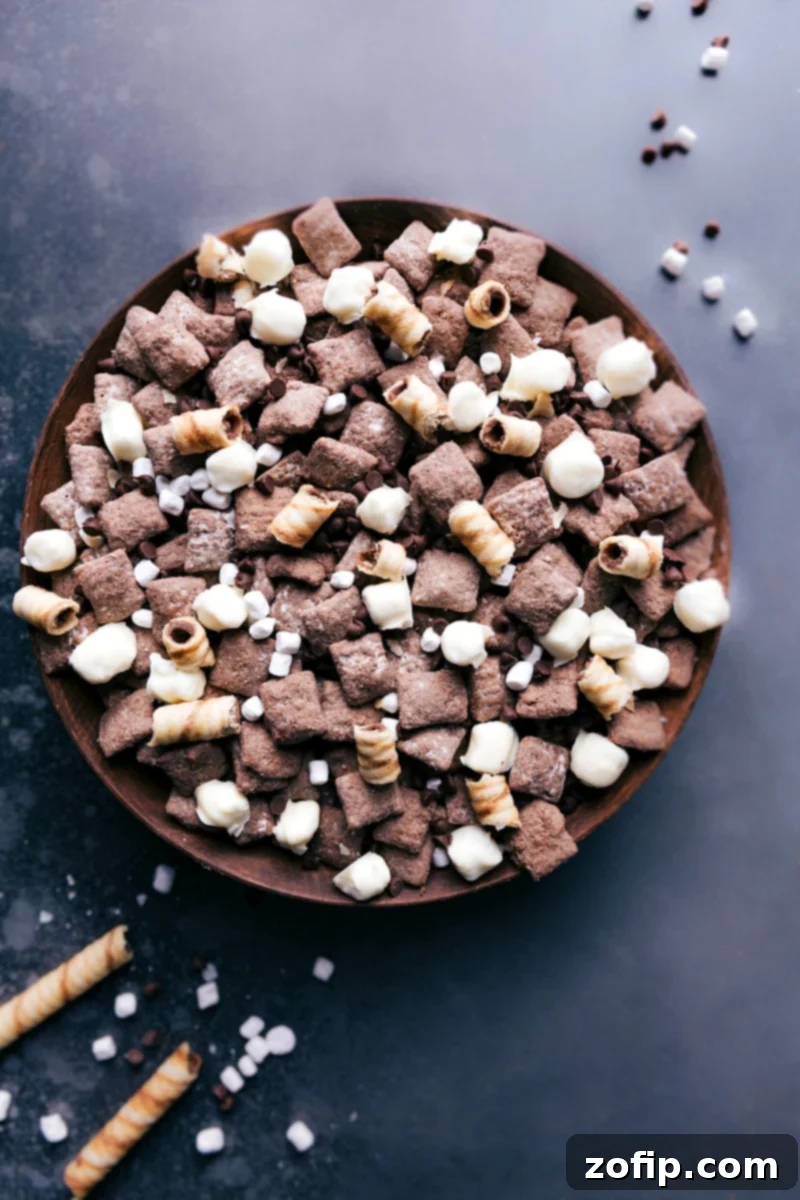 A bowl overflowing with delicious Hot Chocolate Snack Mix, featuring chocolate Chex, marshmallows, and chocolate chips.