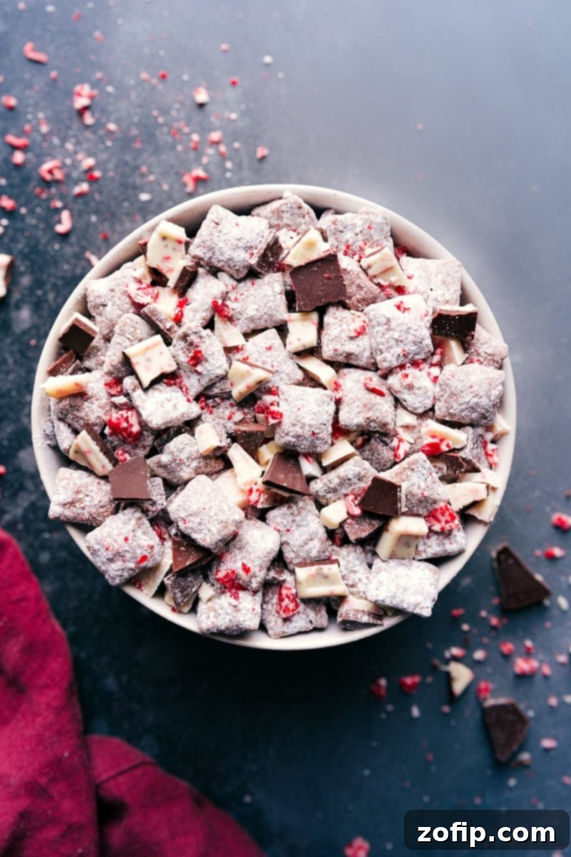 A large bowl brimming with festive Peppermint Bark Muddy Buddies, generously coated in a delicate layer of powdered sugar and finely crushed peppermint pieces, ready to be enjoyed as a delicious holiday snack.