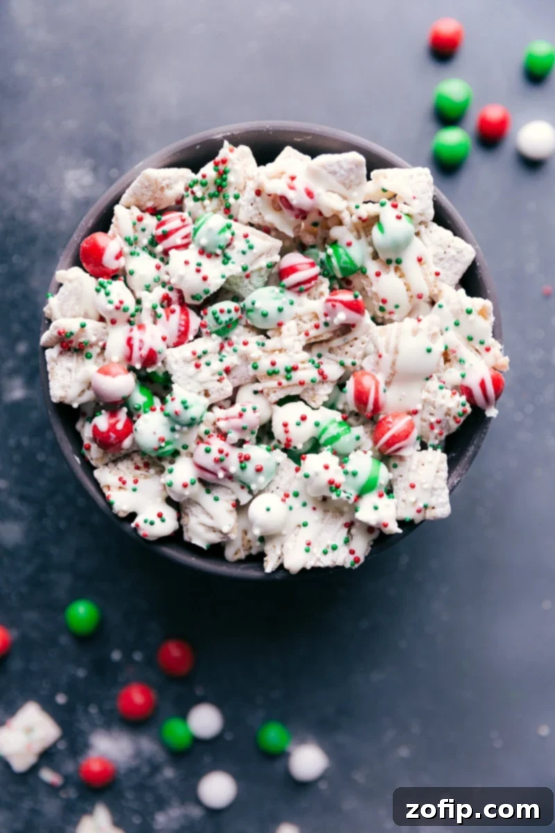 Overhead view of a bowl filled with Sugar Cookie Snack Mix, showing cereal, M&M's, white chocolate drizzle, and colorful sprinkles.