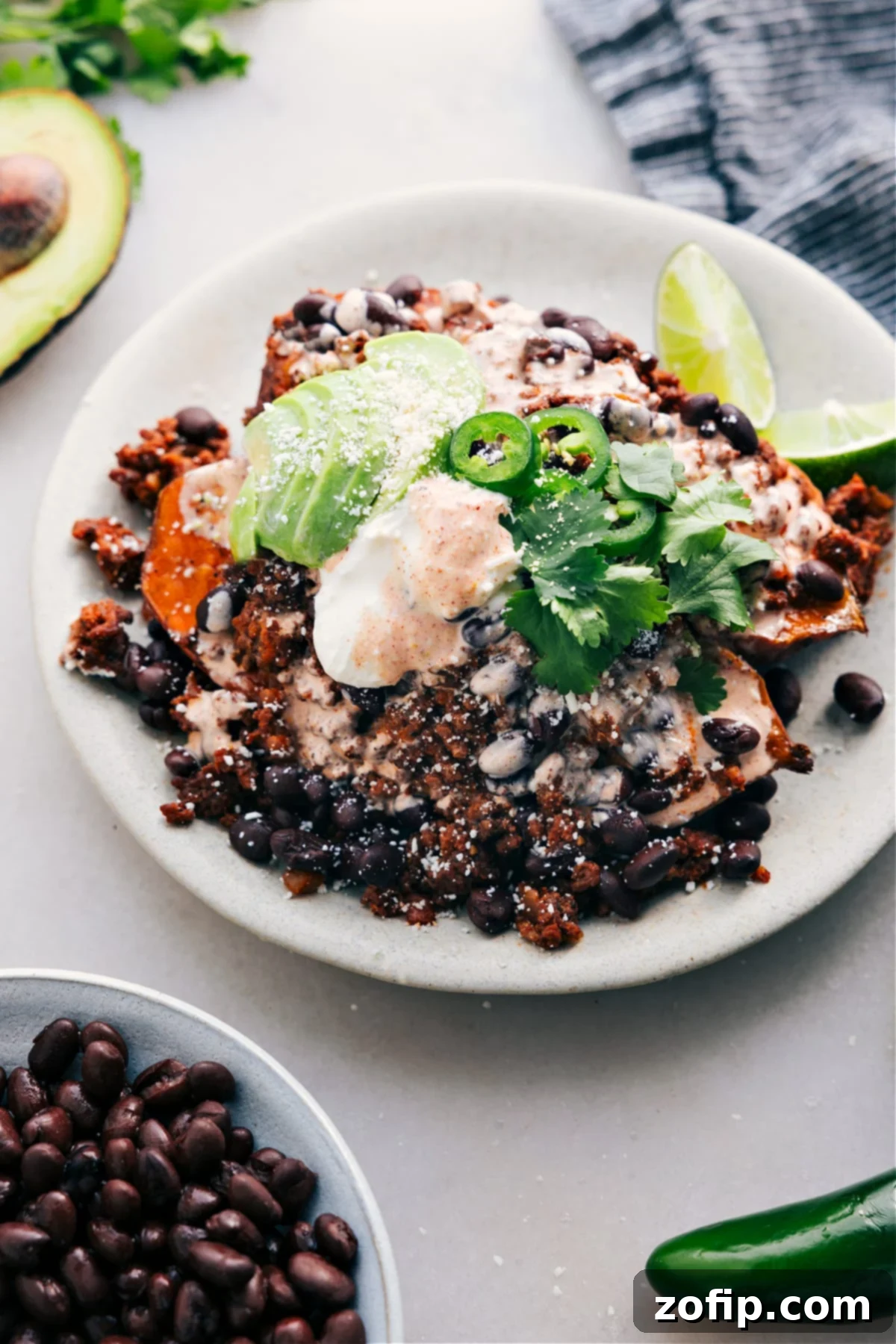 Taco Stuffed Sweet Potatoes are served on a plate and loaded with meat, avocado, sauce, jalapeño, and fresh cilantro, showcasing a vibrant and appealing meal.