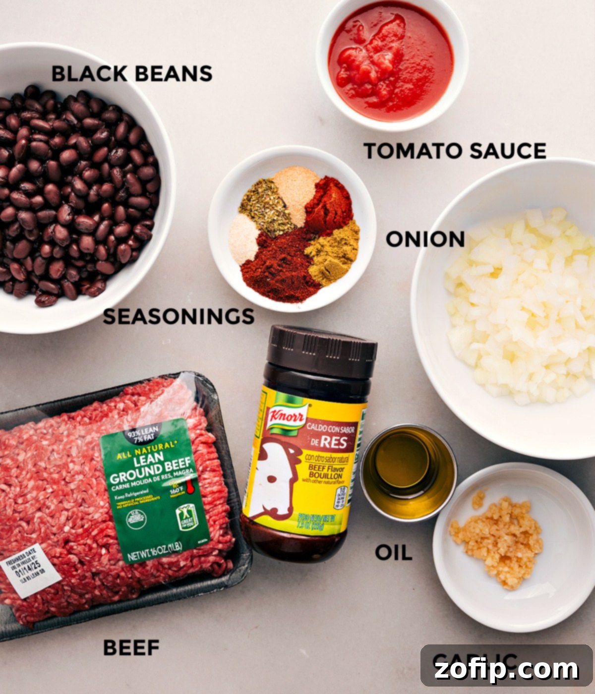 All the ingredients for this recipe are prepped and ready for easy assembly, including tomato sauce, ground beef, diced onion, black beans, a selection of seasonings, olive oil, and minced garlic.