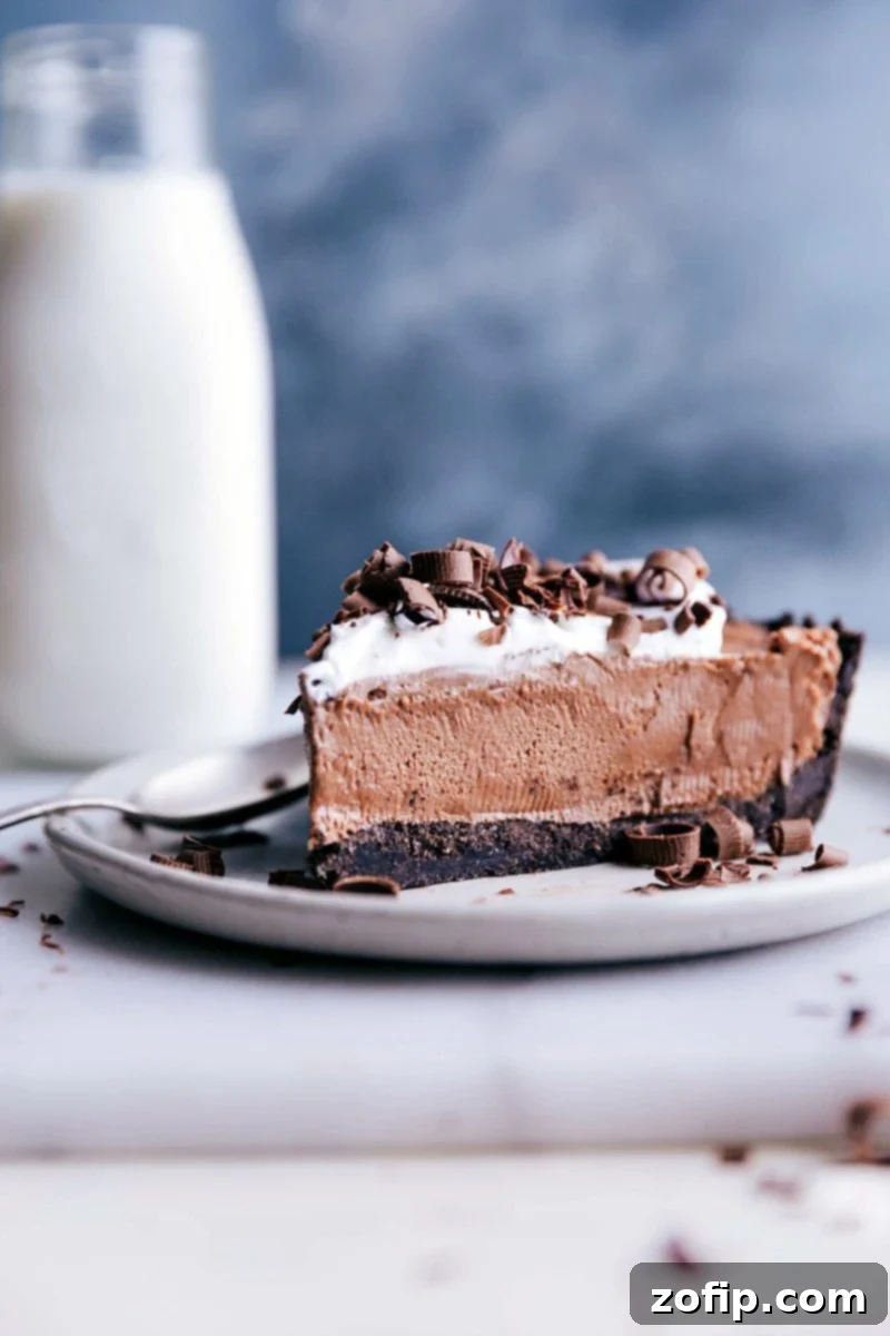 A decadent slice of no-bake Nutella pie, crowned with fluffy whipped cream and elegant chocolate shavings, presented on a plate with a spoon, inviting a delightful taste.