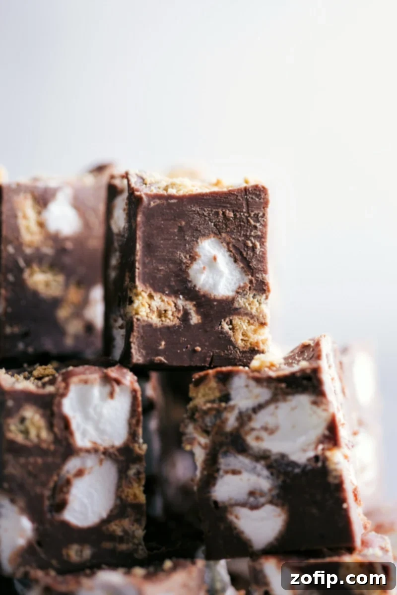 Delicious Easy Stovetop S'mores Fudge with milk chocolate, graham crackers, and marshmallows. Perfect holiday or anytime treat! Close-up image of several squares of rich S'mores Fudge, showcasing the gooey marshmallows and crunchy graham cracker pieces embedded in the chocolate.