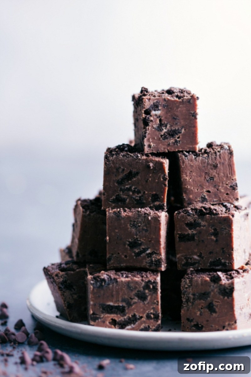 A stack of rich, homemade Chocolate-Covered Oreo Fudge pieces, showcasing the creamy chocolate base and visible crushed Oreo cookie chunks. Perfect for holiday dessert tables.
