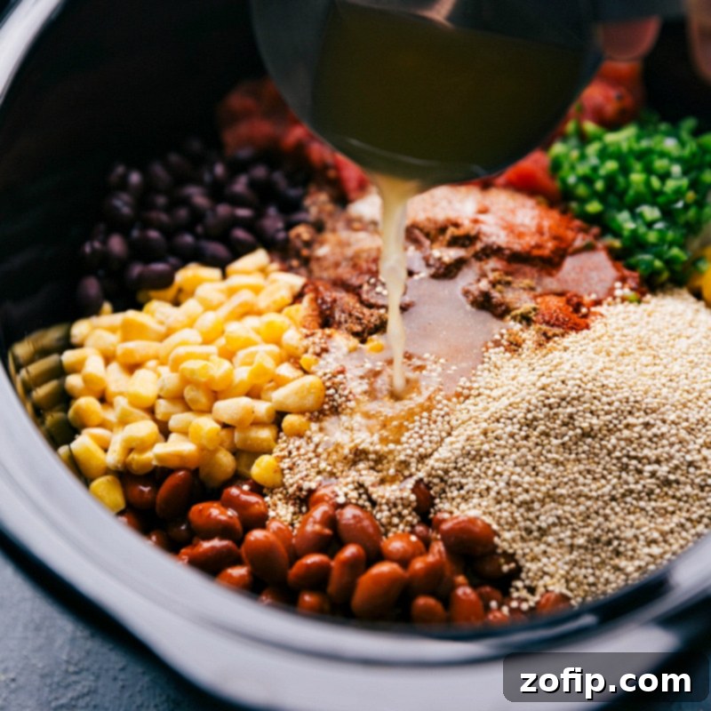 A careful hand pouring vegetable stock into a slow cooker that is already filled with a colorful medley of quinoa, beans, and various vegetables for Crockpot Quinoa.