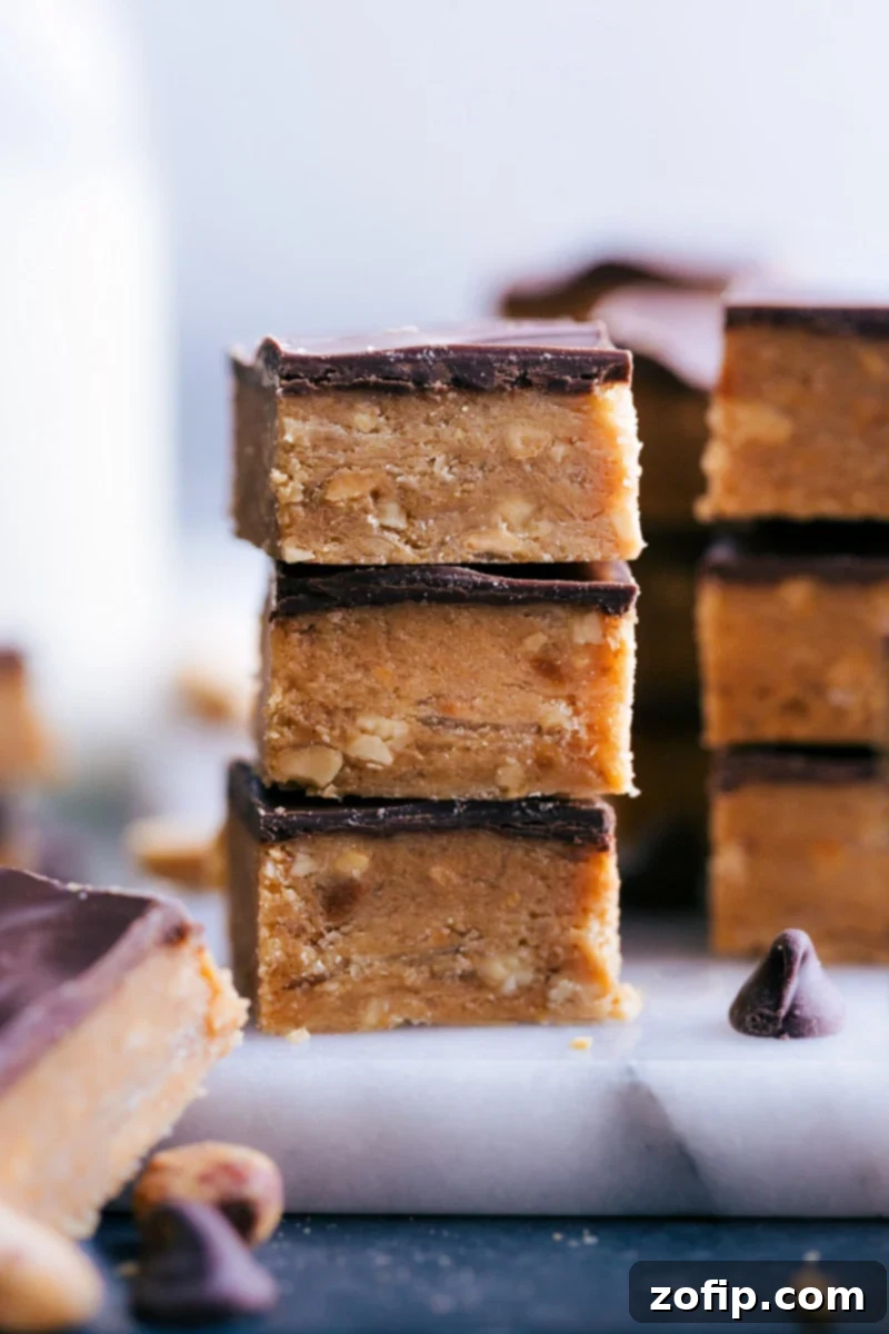 Several pieces of homemade Peanut Butter Crunch Candy stacked on a wooden board, glistening with chocolate topping.