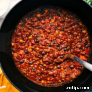 Hearty Turkey Chili 3 A close-up of a steaming bowl of Turkey Chili, generously topped with shredded cheddar cheese, a dollop of sour cream, and fresh cilantro, promising a delicious and comforting meal.
