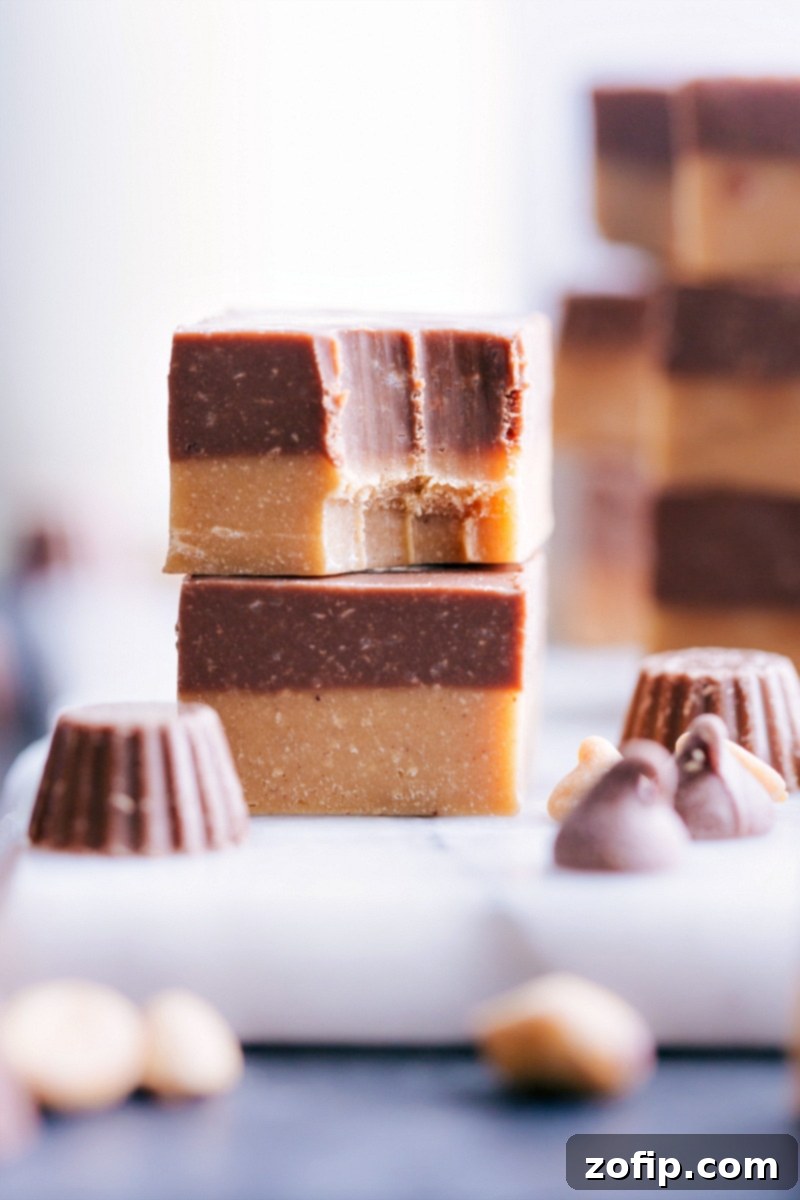 Delicious two-layered Reese's Fudge, showcasing the peanut butter and chocolate layers. An easy, no-thermometer recipe. Image of two pieces of Reese's Fudge stacked, one with a bite taken out, showing the perfect layers.