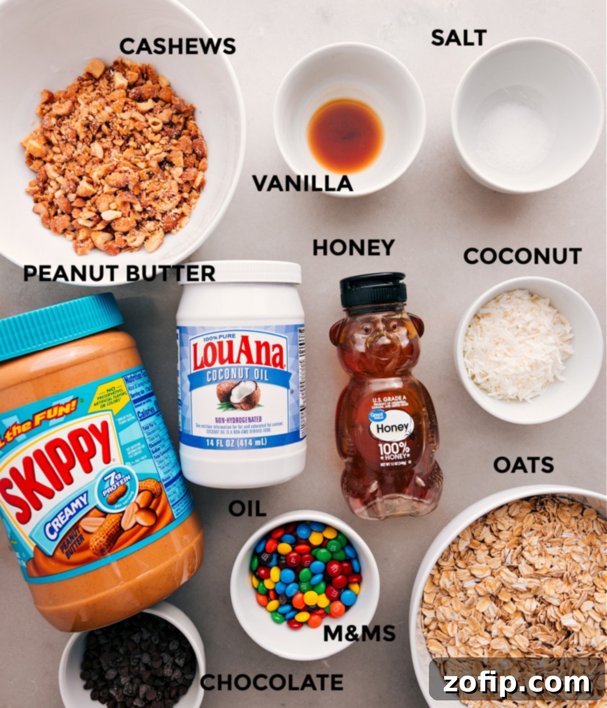Ingredients In Chewy Granola Bars A vibrant display of all fresh ingredients for chewy granola bars: oats, cashews, honey, peanut butter, M&M's, chocolate chips, coconut oil, vanilla, and salt.