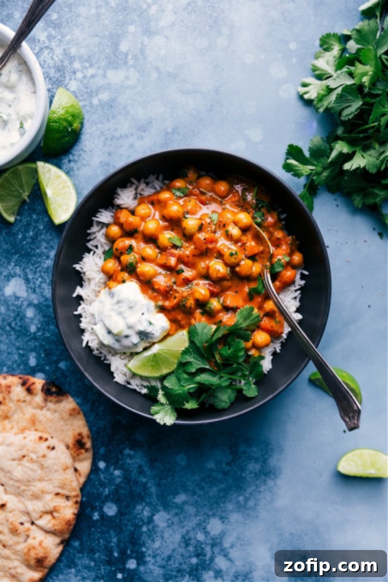 A vibrant bowl of Chickpea Curry, garnished with fresh cilantro, served alongside fluffy basmati rice, warm naan bread, and a cooling cucumber raita.