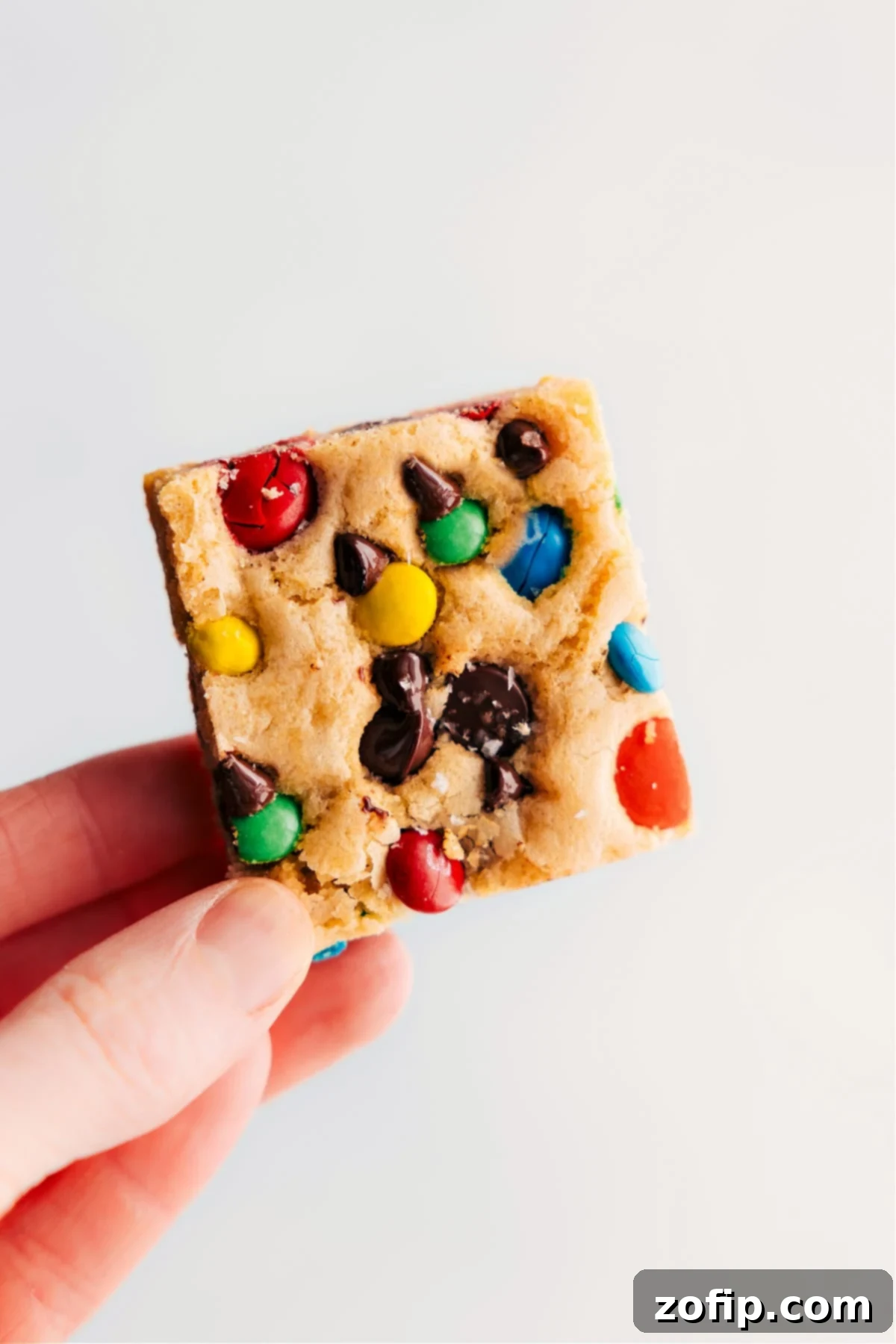 Delicious M&M Cookie Bars being held up, showcasing their vibrant colors and chewy texture.