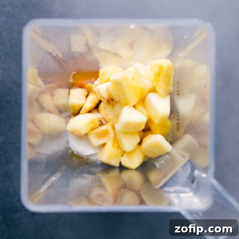 A high-angle shot inside a blender, showcasing a mix of vibrant frozen pineapple chunks, creamy vanilla ice cream, and golden pineapple juice, all ready to be transformed into a smooth, refreshing Dole Whip.