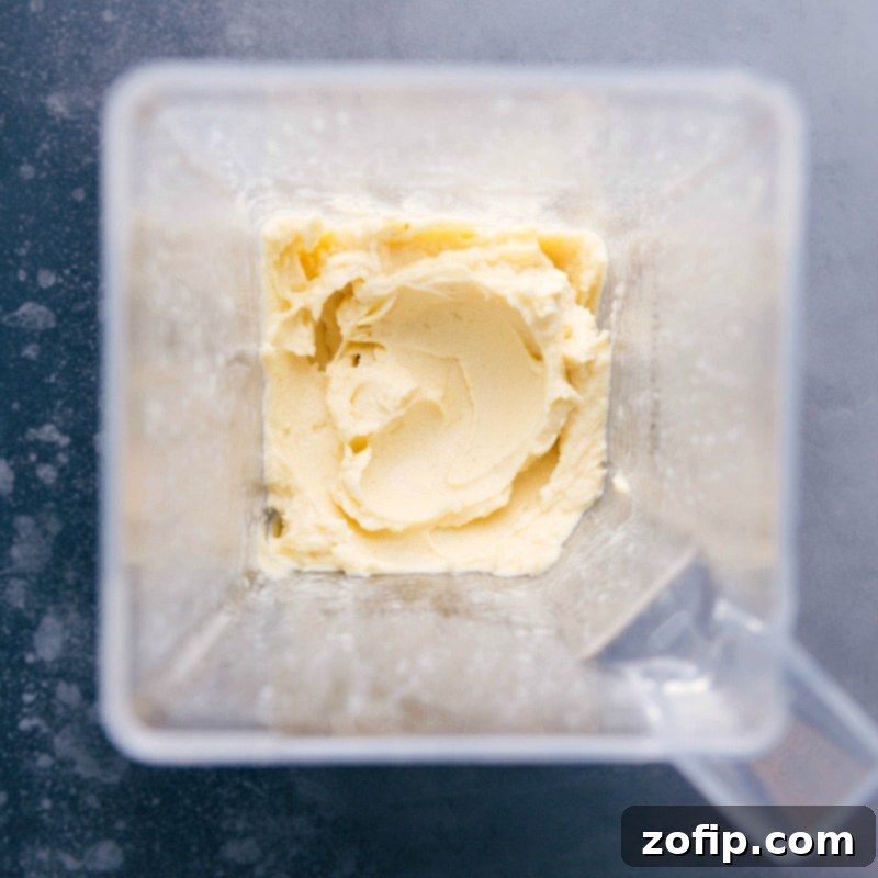 A top-down view of a blender jar filled with a thick, pale yellow, and perfectly smooth pineapple mixture, ready to be served as homemade Dole Whip.