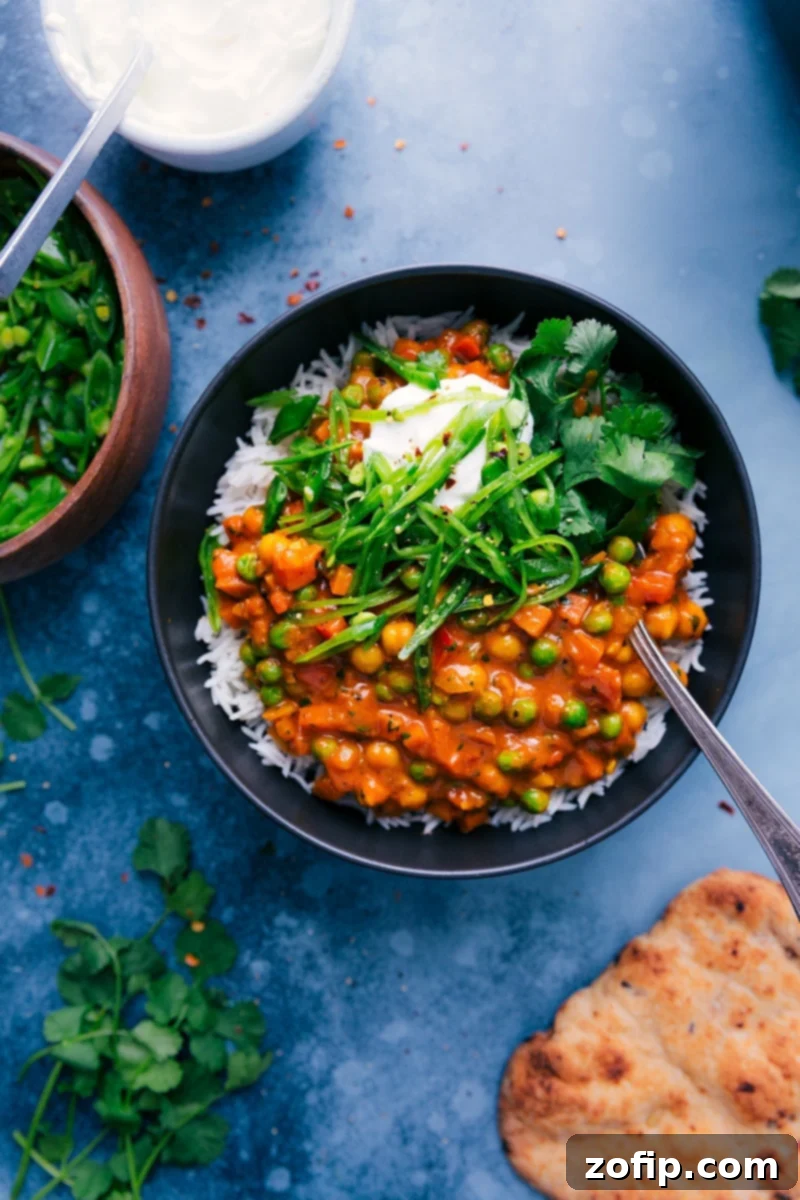 A vibrant bowl of Vegetarian Tikka Masala garnished with fresh snap peas, a swirl of Greek yogurt, and fragrant cilantro, ready to be enjoyed.