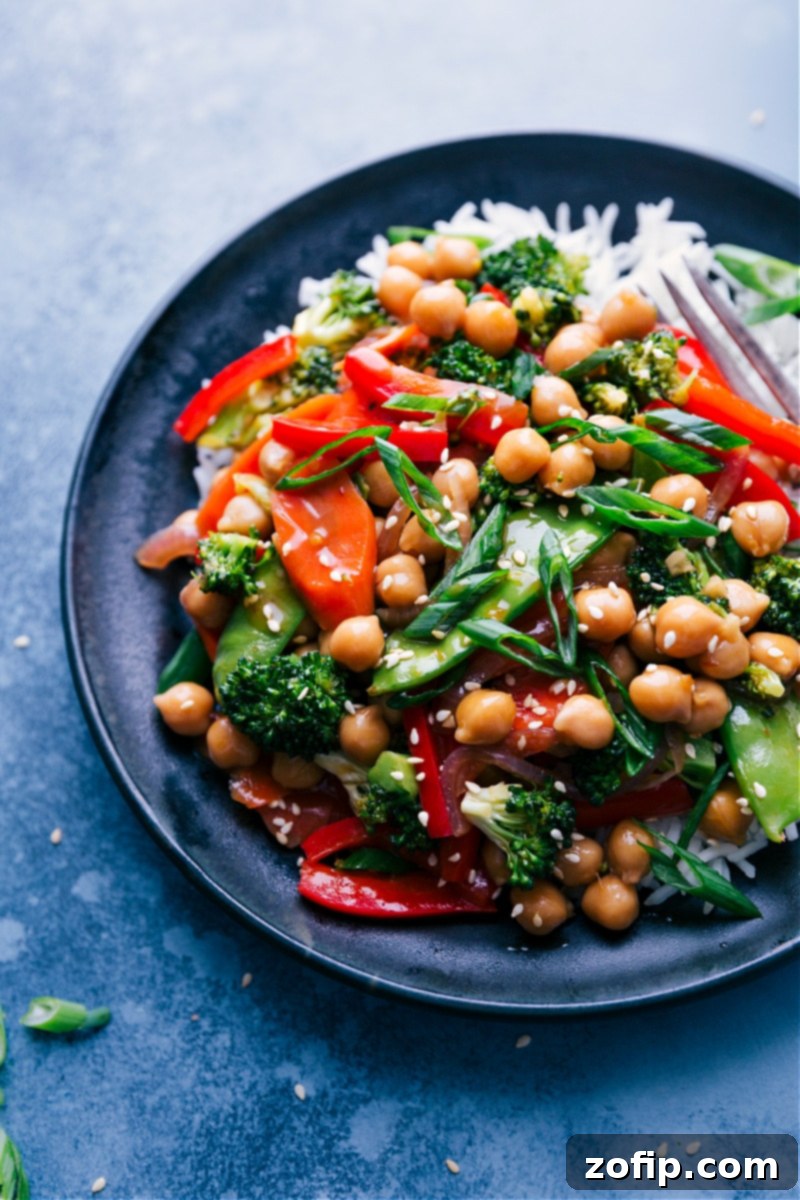 A plate of General Tso Chickpeas served over white rice, ready to eat, garnished with green onions and sesame seeds.