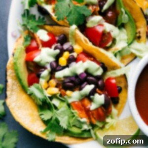 Finished BBQ chicken tacos topped with vegetables, beans, cilantro, and creamy dressing, ready to serve.