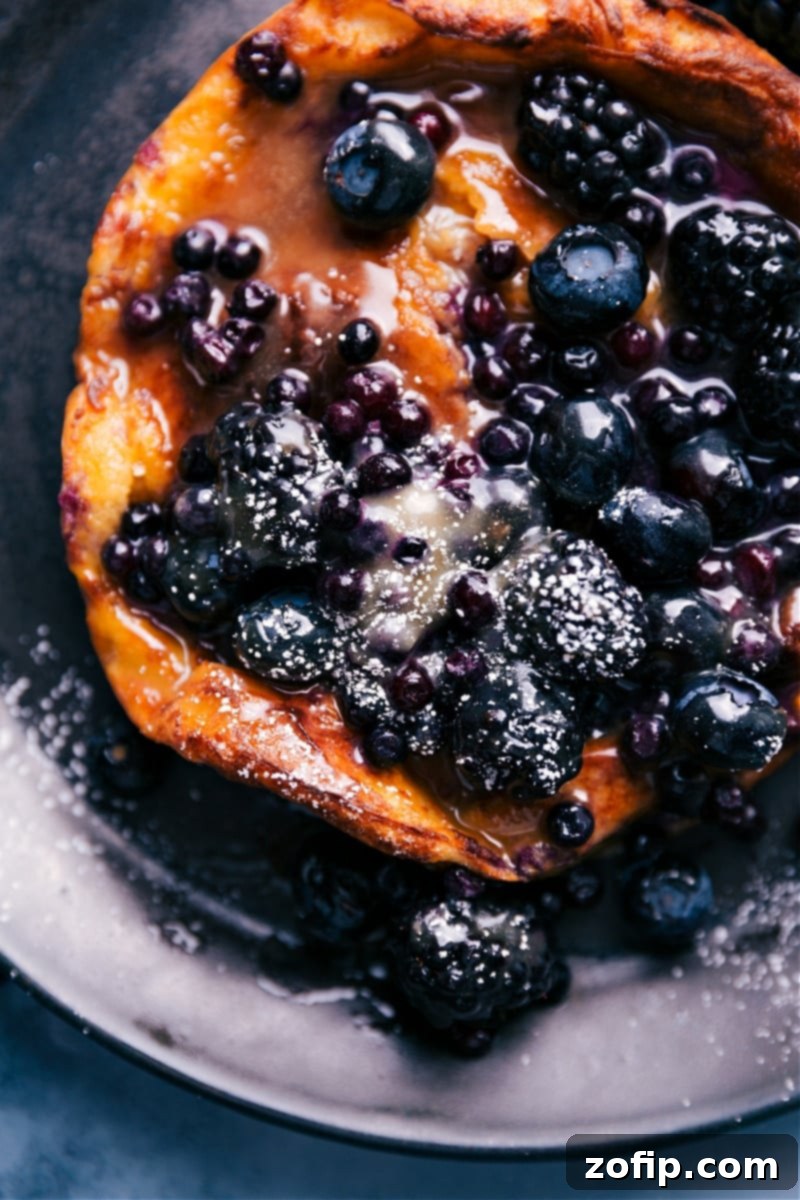 A stunning overhead shot of an Air Fryer Dutch Baby, showcasing its impressive rise and perfect golden finish, ready for delicious toppings and serving. Overhead view of a beautifully puffed Air Fryer Dutch Baby pancake, generously garnished with powdered sugar and an assortment of fresh berries.