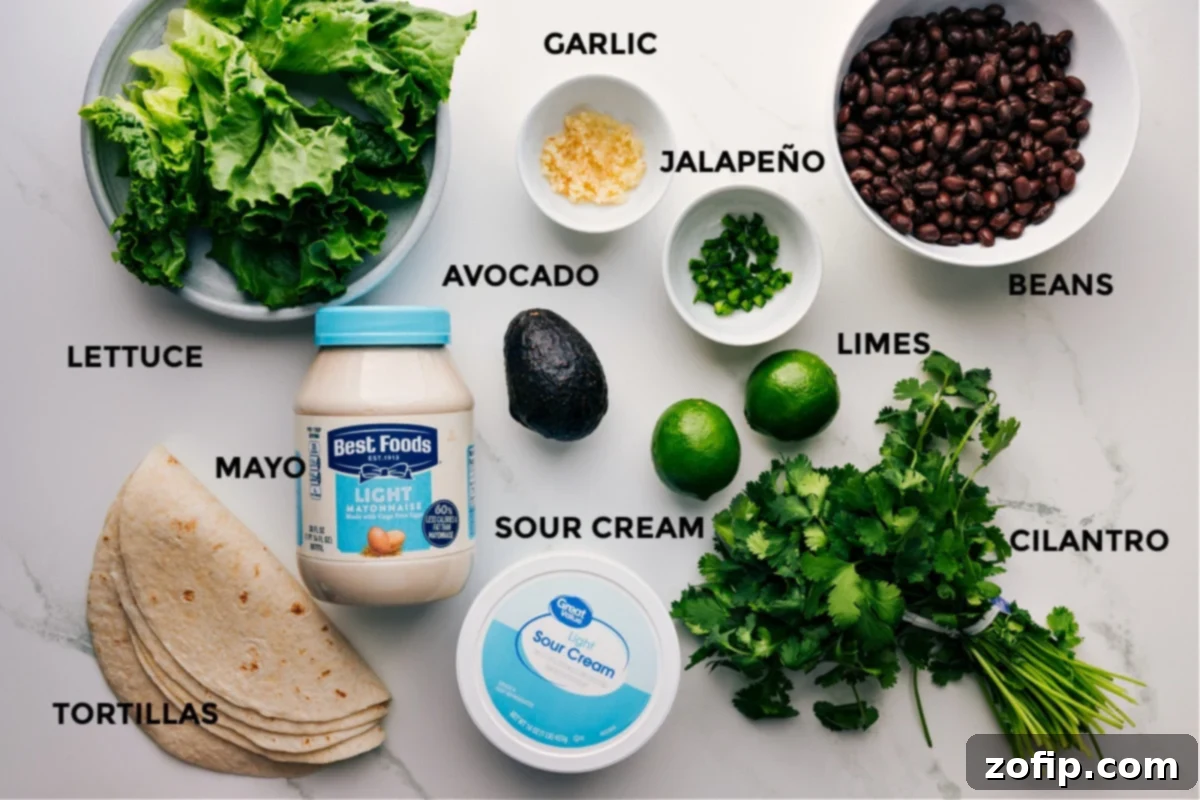 A vibrant display of fresh ingredients for making homemade Black Bean Wraps, including crisp lettuce, perfectly ripe avocados, juicy limes, canned black beans, creamy sour cream and mayonnaise, fresh cilantro, and soft flour tortillas.