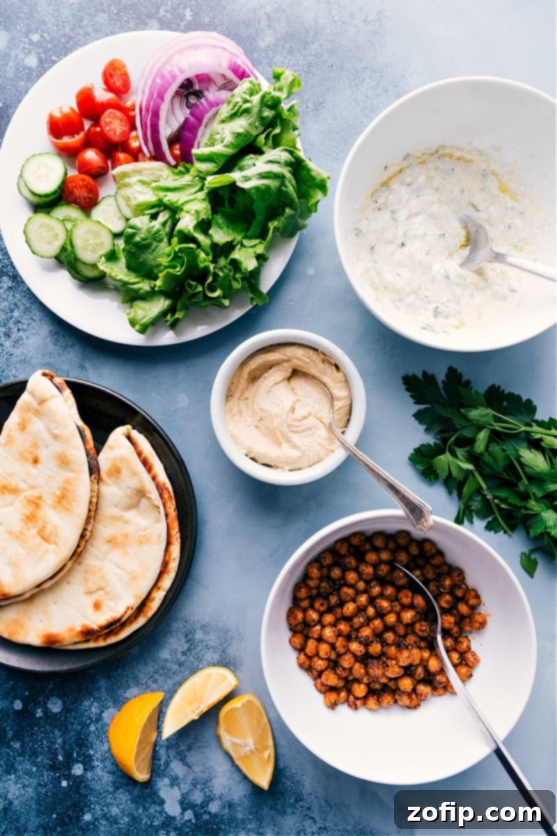 Vegetarian Gyros--they're loaded with robustly-seasoned and perfectly roasted chickpeas, a medley of veggies, and our favorite Tzatziki sauce. This easy, weeknight meal can be ready in about 30 minutes or less if you’ve got an air fryer! #dinner #healthy #whole #whole30 #best #quick #easy #simple #greek #vegetarian #gyros Overhead view of fresh ingredients for Vegetarian Gyros, including chickpeas, pita bread, various vegetables, and tzatziki sauce.