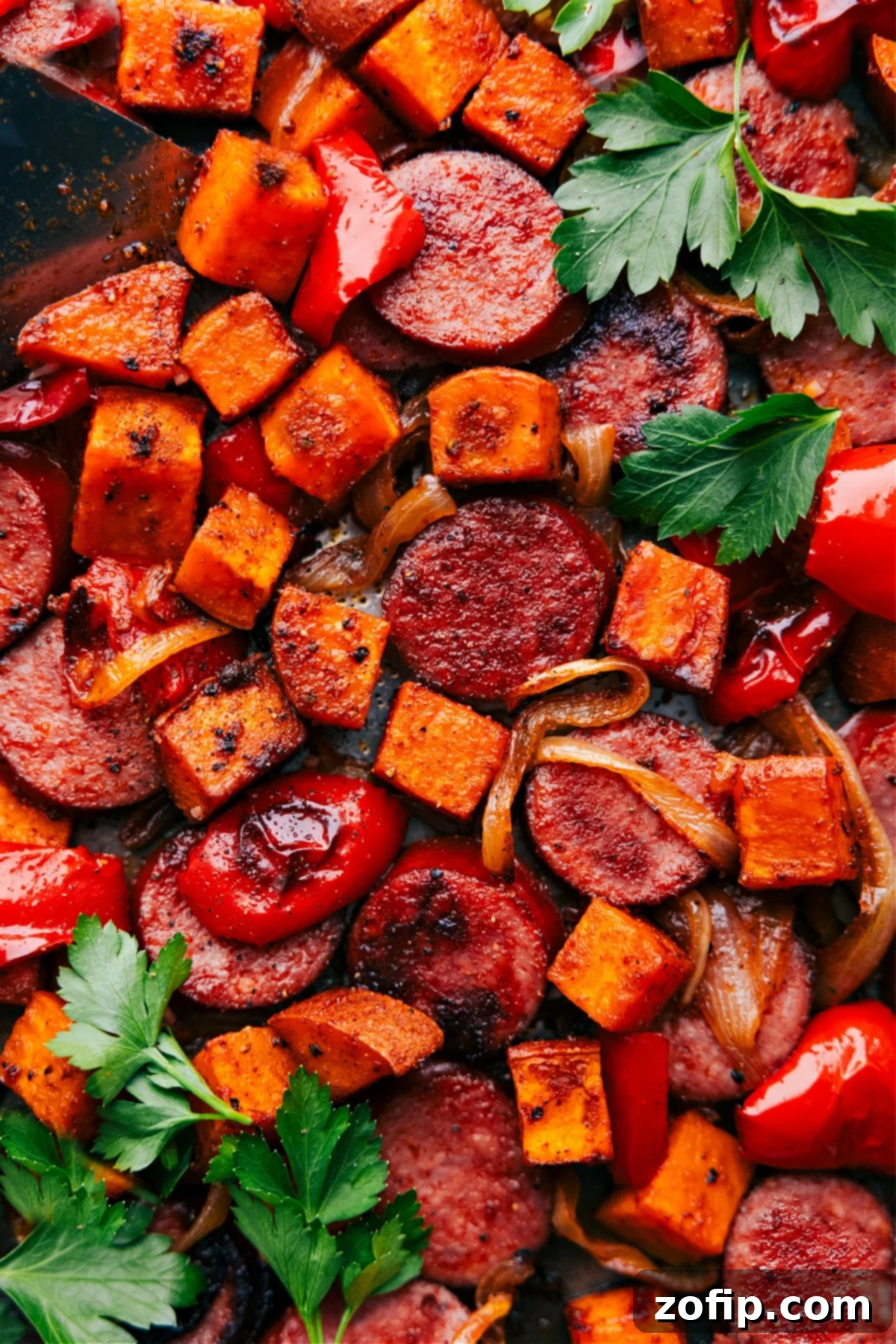 Golden brown roasted sweet potato and smoked sausage fresh out of the oven, piled on a single baking sheet, ready to serve.