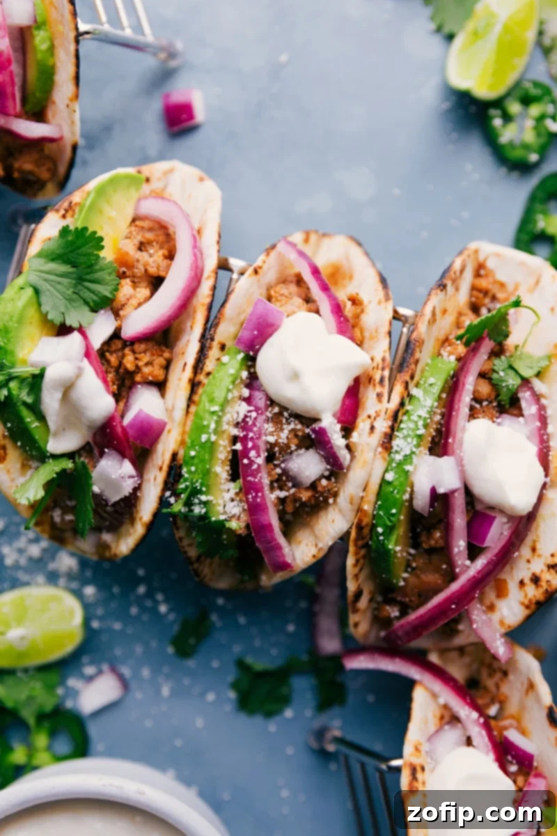 Close-up of three beautifully assembled Ground Pork Tacos with fresh toppings and lime crema.