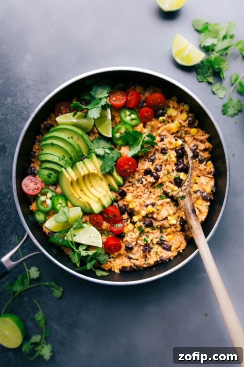 Delicious one-skillet Mexican Chicken and Rice in a large pan, topped with fresh avocado slices, cilantro, and a lime wedge, ready to be served.
