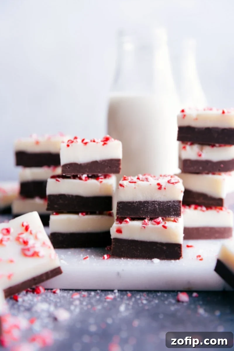Stacked squares of rich Peppermint Fudge, showcasing the distinct chocolate layers and festive candy cane topping.