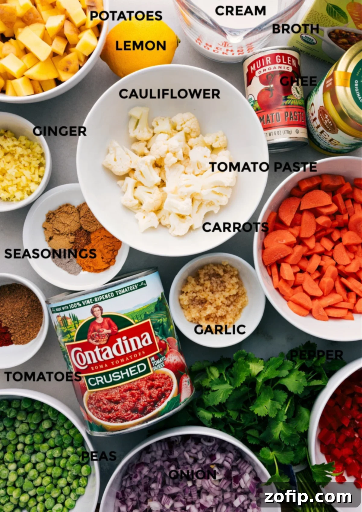 Assortment of fresh ingredients for Vegetable Masala, including diced red onion, carrots, bell pepper, gold potatoes, cauliflower florets, minced garlic, ginger, tomato paste, fire-roasted crushed tomatoes, vegetable broth, heavy cream, frozen peas, and a blend of aromatic spices like turmeric, coriander, paprika, garam masala, cumin, and cardamom.