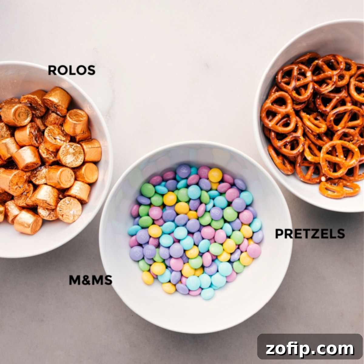 Essential ingredients for Easter Pretzels: pretzels, unwrapped chocolate candies, and pastel M&Ms, neatly arranged for preparation.