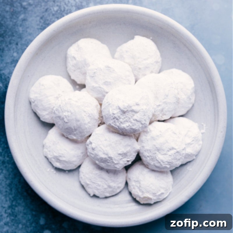 A charming close-up shot of a plate elegantly piled high with delicate, perfectly round Mexican Wedding Cookies, generously dusted with powdered sugar, emphasizing their pristine 'snowball' or 'bunny tail' appearance for Easter gifting.