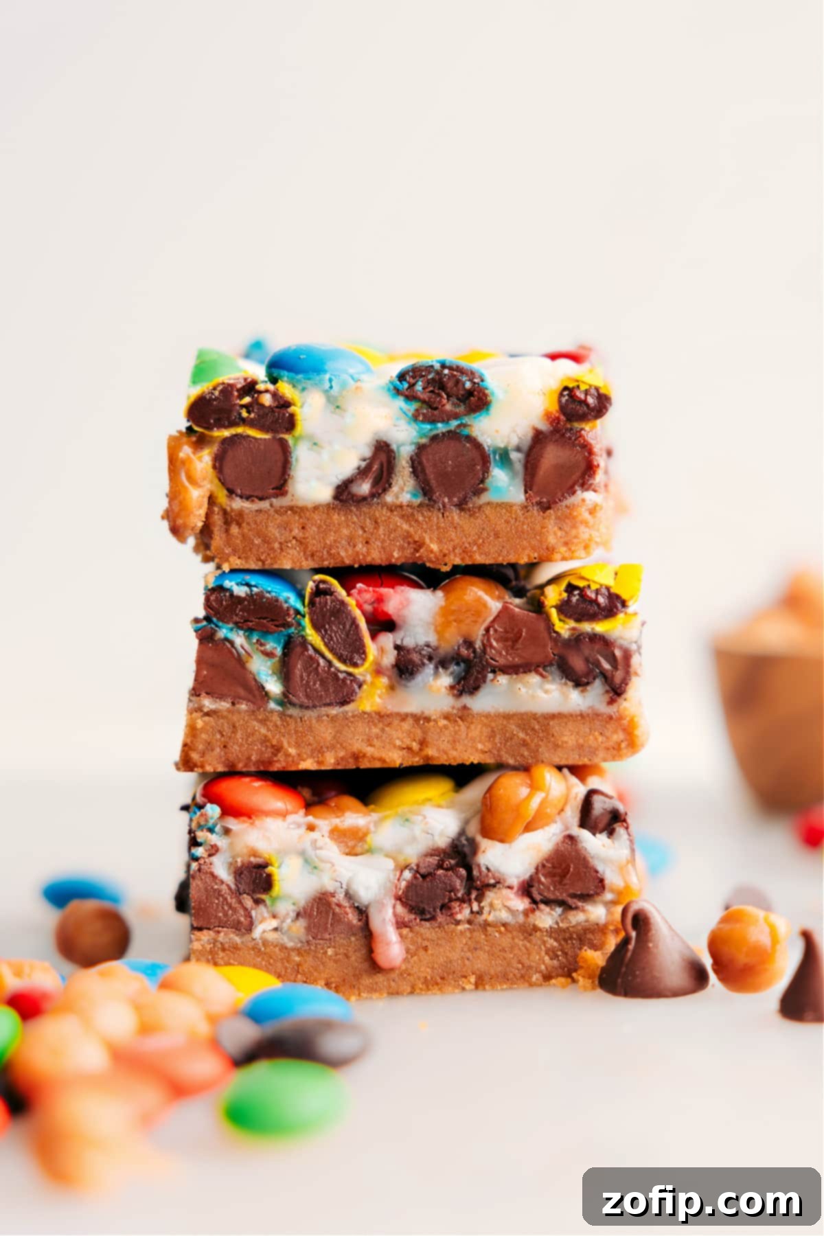 Classic Magic Cookie Bars, layered with graham cracker crust, chocolates, M&Ms, caramel, and oats, stacked invitingly on a cooling rack.