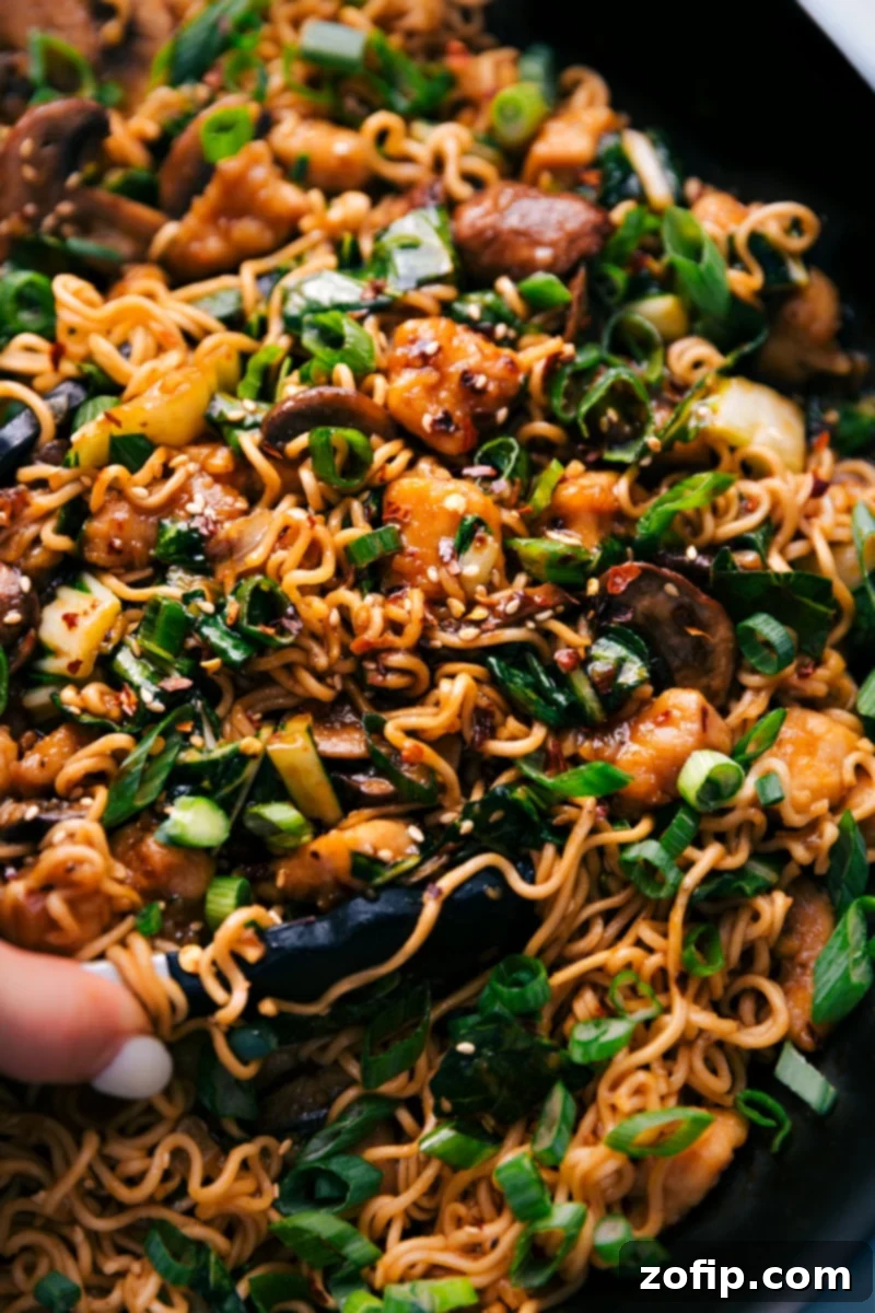 General Tso Ramen in a pot with tongs taking out a bit, highlighting the rich sauce and noodles