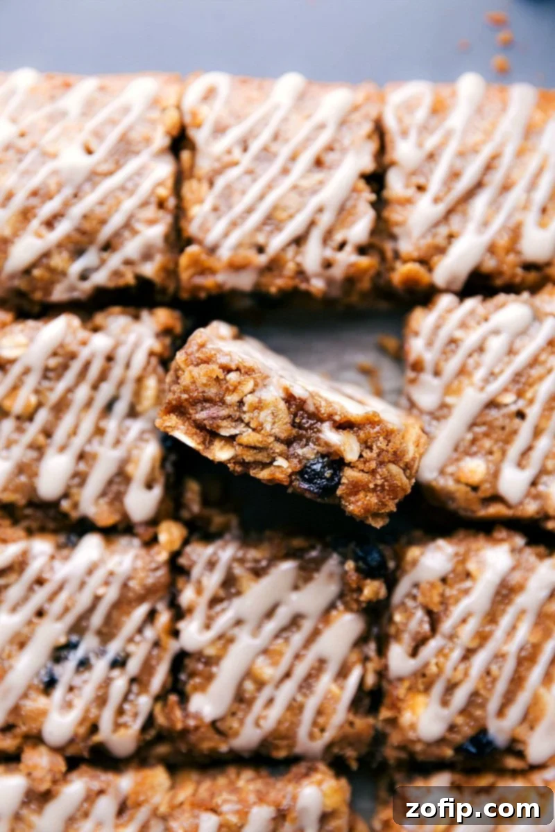 Image of the blueberry oatmeal squares cut in squares with one of them sitting up showing the inside, showcasing its soft, chewy texture and delicious blueberries.