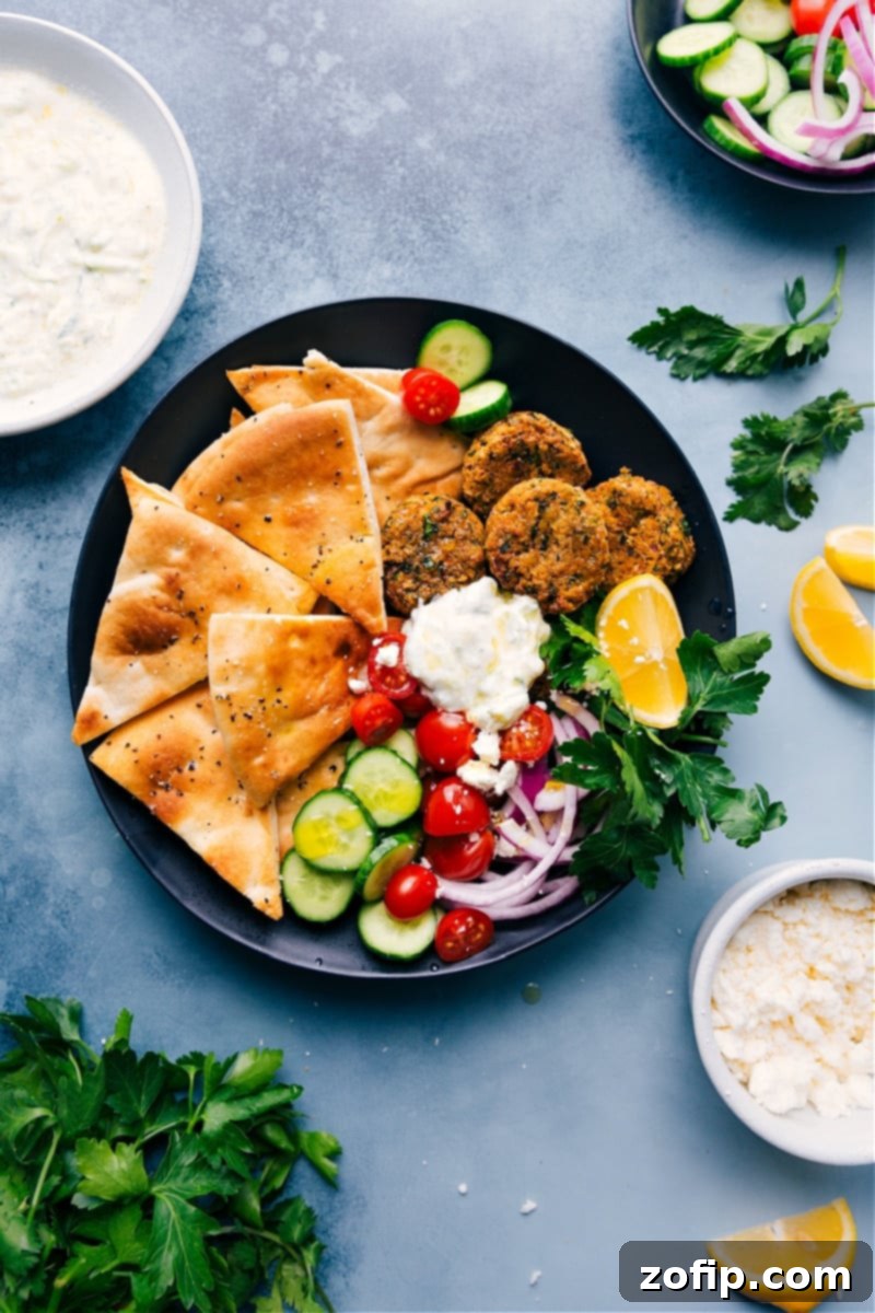 A plate filled with golden Air Fryer Falafels, toasted pita triangles, and a creamy tzatziki sauce, surrounded by fresh cucumber and tomato slices.