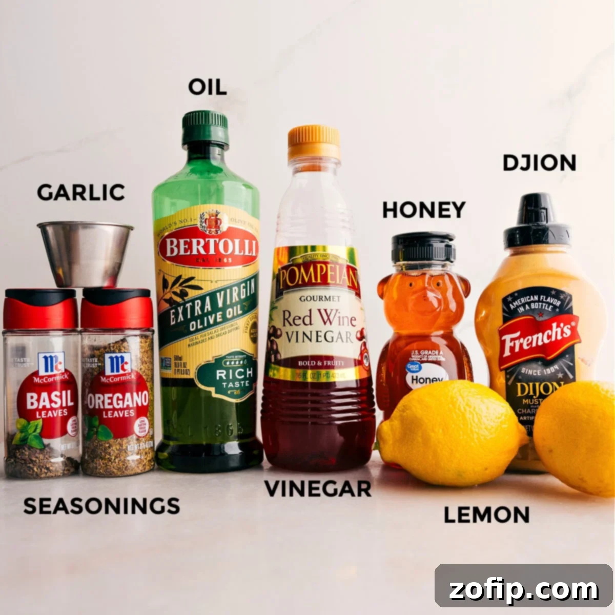 A collection of fresh ingredients laid out for the zesty lemon dressing of this sweet potato quinoa salad, including olive oil, red wine vinegar, honey, Dijon mustard, fresh lemon, minced garlic, and various dried seasonings.