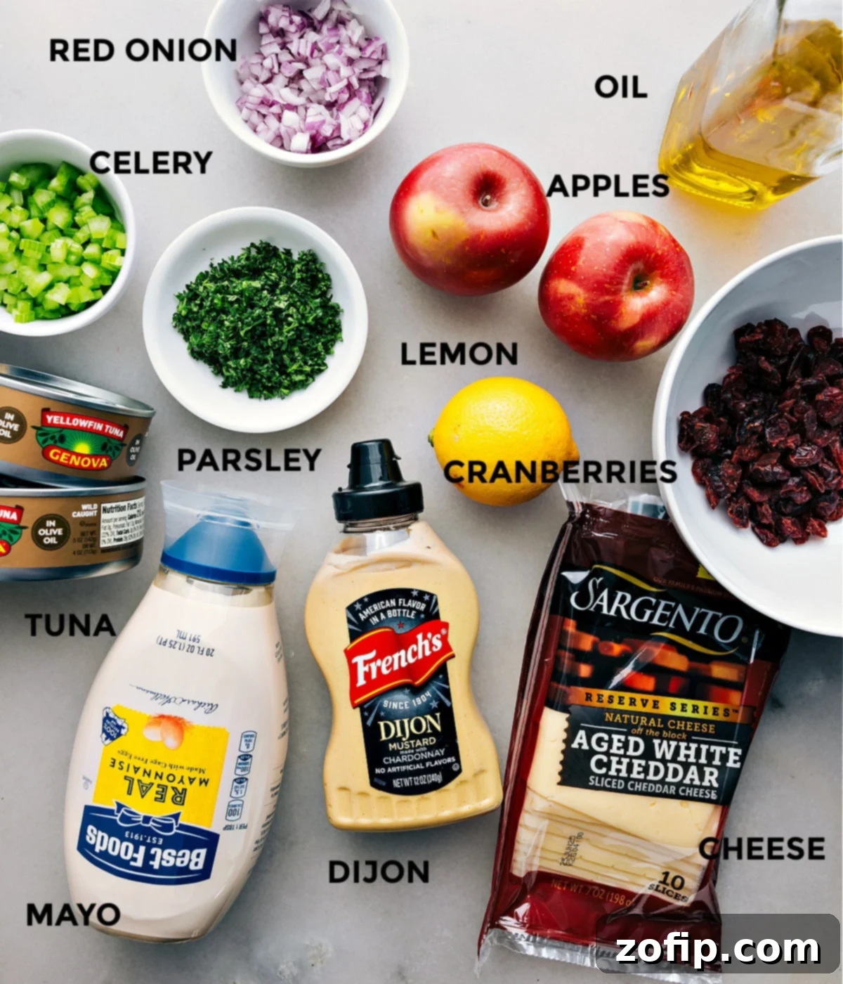 All the fresh ingredients for this easy tuna salad recipe, including oil-packed tuna, dried cranberries, lemon, olive oil, red onion, celery, parsley, cheddar cheese, Dijon mustard, and mayonnaise, prepped and ready for quick assembly.