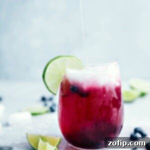 Frosted Lime-Berry Spritzer served in a glass with a sugared rim, lime, and blueberries.