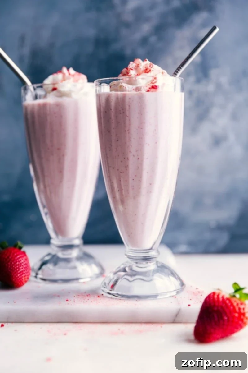 Two strawberry milkshakes, topped generously with fluffy whipped cream and adorned with colorful straws, showcasing a thick, inviting, and utterly delicious dessert. Perfect for a refreshing and indulgent treat.
